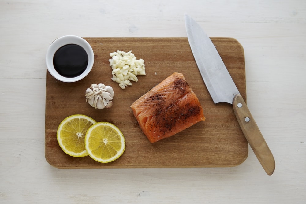 gray knife and orange fish on wooden chopping board